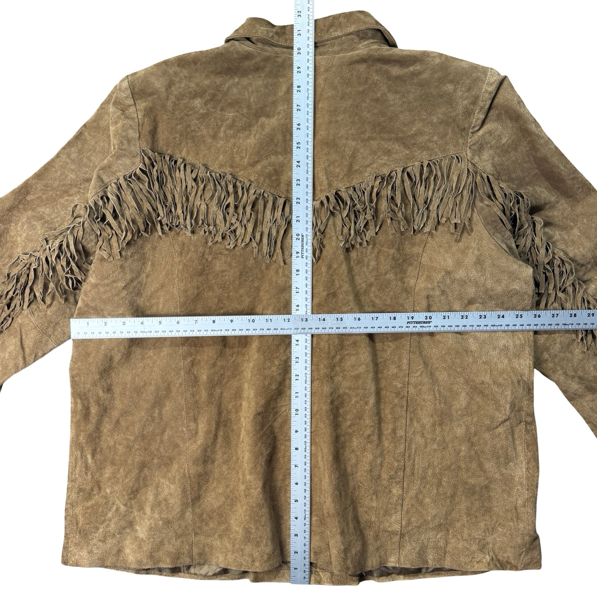 Tan suede fringe jacket laid flat with measuring tape