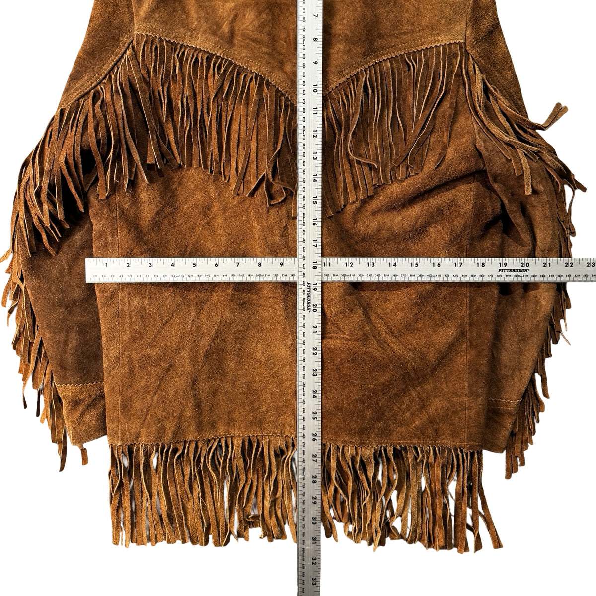 Brown suede fringe jacket laid flat with measuring tape